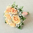 Resting gently atop a subtly textured oatmeal fabric, this round hand-tied bouquet radiates understated New Barnet elegance. At its heart, seven to nine plush peach roses reveal gracefully unfurling petals-each bloom a lush swirl of soft apricot and warm coral tones. Weaving between the roses are abundant clouds of delicate white baby's breath, offering a dreamy airiness and striking contrast alongside the blooms' rich hues. Sprigs of dark green leaves slip from beneath the flowers, providing depth and a natural frame that recalls strolls through leafy local parks like Friary Park. The bouquet's stems are gathered in a smooth, light coral satin ribbon handle, lovingly adorned with a spiral of tiny white pearls-an emblem of sophistication and personal attention familiar to New Barnet's cherished family celebrations. Illuminated by an even, gentle light, every detail stands out: from the pinpoint shine of the pearls to the soft textures of the petals and the crisp finish of the stems' cut bases. Perfect for weddings or momentous occasions in New Barnet, this bouquet embodies romantic hope and refined artistry, exemplifying the care and tradition local florists bring to every celebration.