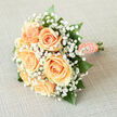 This bridal bouquet reads like a small poem of spring: blushing peach roses gathered closely so their creamy centers glow, surrounded by a froth of pure white gypsophila that softens every edge. Each rose looks freshly opened, petals layered in a gentle spiral and catching light with a soft satiny sheen. The baby's breath acts like a delicate mist, filling the negative space with tiny points of white that diffuse and amplify the bouquet's luminosity. Interspersed glossy green foliage lends contrast and depth, the darker leaves providing a reassuring frame for the pale florals and helping the peach tones read warmer and more defined. The stems are bound in a peach satin ribbon, smoothed and secure for comfortable carrying, and the finish is a string of small pearls-hand-placed to reflect points of memory and quiet celebration. The scent is subtle and pleasing, a cool floral note rather than anything cloying, evoking the feel of a gentle spring morning in Brunswick Park or a calm moment on East Barnet Road before the ceremony. Prepared with a florist's care, this arrangement suits a bride who prefers tradition with a soft contemporary edge, and it travels well for local deliveries across New Barnet and surrounding streets. As delivered by Flowers New Barnet, the bouquet balances refined simplicity with tactile richness: the silkiness of petal, the crispness of baby's breath, the tactile smoothness of ribbon and pearl, all composed to sit lightly in the hand and to photograph with timeless grace.