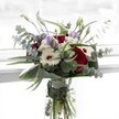 This radiant bouquet, designed with a keen eye for both contrast and harmony, stands in a clear glass vase catching the natural light typical of New Barnet's bright mornings. Vibrant crimson roses provide a passionate focal point, while pure white gerberas with bold, dark centres radiate an uplifting brightness matched only by the open spaces of nearby Oak Hill Park. Pale lilac lisianthus blooms and their elegant buds form gentle accents, threading through the bouquet with a breezy softness that speaks to new beginnings or cherished memories. Airy clusters of white filler flowers add depth and a whispery allure, evoking the calm of a peaceful walk through local neighbourhood lanes. Eucalyptus branches, recognisable by their cool silvery-green leaves, stretch gracefully around the bouquet, infusing the arrangement with subtle aromatics and a hint of contemporary style. At the base, deep green leaves are folded artfully to frame the flowers, providing a vibrant contrast and lending a touch of modern elegance. The vase's transparent quality reveals fresh, water-submerged stems-evidence of local freshness and care. Ideal for expressing gratitude, marking milestones, or simply bringing a slice of natural grace into a New Barnet home, this bouquet is a celebration of colour, scent, and artistry, expertly curated for memorable delivery across the neighbourhood.