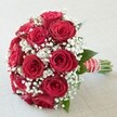In this radiant bridal bouquet, passion and tenderness meet with every petal-a showcase of artistry beloved by wedding couples across New Barnet. An abundant cluster of deep red roses, each plush and velvety, forms a compact, rounded arrangement that draws the eye and stirs the heart. Nestled between the blooms, white baby's breath (Gypsophila) creates gentle puffs of lightness, evoking quiet, hopeful moments walking through nearby green spaces like Oak Hill Woods. The natural vibrancy of the roses is heightened by subtle accents of dark green leaves, peeking through to balance the bold reds and luminous whites. Binding the bouquet is a luxurious red satin ribbon, accented by crisp horizontal white stripes and a delicate spiral of pearls-an elegant finish reminiscent of thoughtful wedding accessories found in New Barnet's beloved boutiques. The stems beneath are freshly cut and exposed, adding a final note of honesty and authenticity to the bouquet's look. Illuminated by soft, even lighting, every detail-petal, pearl, and leaf-comes alive. Ideal for New Barnet ceremonies, local anniversaries, or heartfelt gifts, this timeless floral arrangement tells the story of romance and celebration, capturing the essence of love in flowers that promise beauty, freshness, and meaning for every joyful occasion.