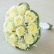 A beautifully composed bridal bouquet lies at a diagonal upon a soft, cream-coloured fabric, evoking the understated elegance of New Barnet's favourite celebration spaces. Central to the arrangement is a tight, full cluster of creamy white to pale yellow roses-each bloom pristine and subtle, petals unfurling in stages of immaculate beauty. Entrancing swathes of delicate white baby's breath (Gypsophila) weave among the roses, their myriad tiny flowers imparting a weightless, airy texture, as if soft clouds drift through the mix. Encircling the flowers, a few skillfully looped, deep green strands of bear grass bring a contemporary twist, perfectly offsetting the pale blooms. The bouquet's stems are bundled with an immaculate white satin ribbon, forming a classic, comfortable handle angled at the right, ready for a bride's gentle hold. The softly blurred background lets every detail shine-the pale roses, the intricate filler flowers, the grace of the greenery-exuding romance, purity, and timeless sophistication. Selected for its refined style and joyful presence, this bouquet is perfect for weddings, anniversaries, or cherished moments in New Barnet, demonstrating the artistry and fresh quality that local florists bring to life's most significant occasions.