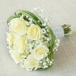 Ethereal in mood and gentle in palette, this bridal bouquet conjures the promises of new beginnings against the subtle backdrop of linen-like beige. Soft white and buttery roses nestle together, their petals unfolding in creamy layers that seem to glow with their own inner light. The fragrance-a blend of fresh rose dew and the delicate, powdery note of gypsophila-feels almost palpable. Billowing tufts of baby's breath drift throughout, suggesting movement and quiet celebration, while slender green arcs of bear grass loop gracefully, framing the composition with fluid, architectural lines. The bouquet's stems, carefully bundled, are enveloped by an opulent silver-grey ribbon, further refined by rows of gleaming white pearls that offer a touch of tactile luxury. Hints of natural stem ends peek through, enhancing the handmade sincerity of the arrangement. This bouquet speaks to heartfelt moments shared in New Barnet, evoking memories of wedding mornings near Monken Hadley Common or anniversary gatherings in local gardens. Distinguished yet tender, the bouquet becomes both a beautiful keepsake and a symbol of the hope and happiness found in the area's most cherished celebrations.