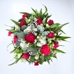 Viewed from directly above against a pristine white background, this lush bouquet appears like a round, living painting, its colours and textures radiating from the centre. Deep crimson red roses are clustered at the heart, some still in tight bud, others beginning to unfurl their velvety petals, suggesting romance and quiet devotion. Around them, vibrant fuchsia and ruby-red carnations ruffle and curl, each petal adding a sense of movement and joyful celebration. Small, daisy-like white spray chrysanthemums nestle between the richer tones, their bright faces bringing clarity and light, much like a clear morning over New Barnet High Street. Threaded delicately throughout are countless tiny white gypsophila blooms, the airy baby's breath forming a soft mist that links each flower together without crowding the eye. Lush greenery frames the composition: strong, pointed dark green leaves, likely from lilies or alstroemeria, give the bouquet structure and a gentle, upward lift, while rounded, silvery-green eucalyptus leaves introduce a cool, contemporary softness. You can almost imagine their subtle, refreshing fragrance, reminiscent of a stroll through nearby Oakhill Park after the rain. The circular, full-bodied shape of the arrangement makes it feel generous and embracing, ideal for birthdays, anniversaries, or a heartfelt get well soon to someone recovering at home in New Barnet. Captured in clear, even light, every petal and leaf appears crisp and freshly arranged, reflecting the care and craftsmanship of a local florist who understands how to balance passion, elegance, and comfort in a single hand-tied bouquet.