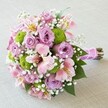 A richly detailed, celebratory bouquet rests on a soft beige cloth, exuding the charm and fresh vibrancy of a special occasion in New Barnet. At its focal point, full-bodied lavender roses bloom with gentle sophistication, their peaceful hues balanced by lively, round button chrysanthemums in zesty lime green-a nod to contemporary floral trends. Breezy sprigs of baby's breath dance through the bouquet, creating an airy, ethereal frame while delicately pink Alstroemerias-streaked with sunlit yellow and deep pink-enhance the palette's romantic depth. The compact, rounded style ensures each flower's colour and texture is showcased, and rich green foliage peeks out to underscore the bouquet's abundance. All stems are neatly wrapped in a lustrous fuchsia satin ribbon, ornamented with petite pearls, a final touch of refinement. Designed with the discerning eye of a New Barnet florist, this bouquet is an embodiment of local artistry and celebration, making it ideal for weddings, engagements, or simply expressing heartfelt joy in the heart of the Barnet community.
