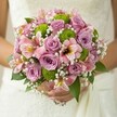 Bathed in gentle daylight, this exquisite bridal bouquet-handcrafted by a New Barnet florist-captures a fresh, enchanting blend of color and emotion. A symphony of lavender and blush pink roses unfurls at its center, each bloom resonating with a soft, timeless fragrance. Resting among the roses, lime green button chrysanthemums pop with youthful energy, their round, textured forms adding a playful modern lift that echoes the spirit of New Barnet's vibrant community. Pink alstroemeria lilies, streaked with maroon and golden yellow, peek gracefully from the ensemble, infusing the arrangement with delicate intrigue and a hint of the exotic. Wisps of white baby's breath gather in gentle, cloud-like clusters, drawing the eye with their airy, ethereal beauty-like the first light of a wedding morning near woodland paths or the gardens sprinkled across New Barnet. Deep green foliage, glossy and structured, frames the colors, giving the bouquet a sense of depth and freshness. The close-up view highlights not just flowers, but craftsmanship-petals gleaming, dewdrops glistening, each detail intentional and heartfelt. More than just a wedding accessory, this bouquet speaks of promises exchanged, sunshine through stained glass, and celebrations unfolding across New Barnet. It's perfect for couples seeking elegance, individuality, and a touch of the local charm that makes every wedding day unforgettable.