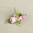 Displayed on a soft, woven linen surface that echoes the inviting textiles found throughout the homes of New Barnet, this elegant boutonniere showcases a central rose in delicate pink, its petals tightly nestled in promise. A ruffled bloom, blush peach in hue with whispers of warm yellow at its center, unfurls nearby, adding a gentle contrast and subtle radiance to the floral composition. Sprigs of white baby's breath lend airy lightness, while vibrant green cushion mums dot the arrangement like lively notes of nature seen in local parks around East Barnet. The array of fresh, glossy foliage-from slim, grass-like reeds arching upward to broader, folded leaves at the base-creates depth and visual interest, while the careful banding of stems with a bright fuchsia satin ribbon bow at the base lends a final flourish of celebration and style. Bathed in diffuse natural light, the arrangement's colors and soft textures are brought to life against the neutral, textured backdrop. Whether carried by a groom, worn by a guest, or pinned on a prom lapel, this meticulously crafted boutonniere evokes the sentiment and freshness of special moments in New Barnet-an exquisite floral accent skillfully created for unforgettable occasions.
