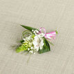 A finely crafted floral boutonniere lies against a pale oatmeal-coloured woven fabric, its calm, neutral background allowing every gentle detail to stand out. The focal flower is a white alstroemeria-like bloom, open and welcoming, its inner petals delicately brushed with reddish-brown speckles that lend depth and personality. Encircling it are small, ivory-white buds and partially opened flowers, reminiscent of campanula or lily-of-the-valley, poised between tight promise and full blossom. Airy sprigs of white baby's breath weave through the design, softening the edges and creating a misty, romantic halo around the central bloom. A cone-shaped, lime-green cluster of tightly packed buds, similar to Ornithogalum, adds a vivid splash of colour and a contemporary, architectural line. Broad, dark green leaves anchor the piece, while fine, looping strands of slender foliage or bear grass arch gracefully, echoing natural growth and giving the boutonniere a fluid, organic rhythm. At the base, a smooth pink satin ribbon wraps the stems and forms a tidy, shining bow, a subtle nod to joy and celebration. The overall impression is one of purity and gentle intention, like something chosen for a New Barnet wedding at a local church, a quiet civil ceremony near High Barnet, or a milestone celebration held in a family home. You can almost imagine the cool, smooth feel of the ribbon between your fingers and the faint, sweet fragrance of fresh blooms prepared that morning by a neighbourhood florist, ready to be pinned close to the heart.