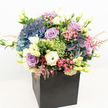 This exceptional floral arrangement, presented in a chic matte black gift bag, epitomises contemporary style with a nod to New Barnet's lush neighbourhoods. Voluminous hydrangeas in shades of blue and periwinkle take centre stage, their rich clusters forming a textured tapestry that recalls the peaceful landscapes near Monken Hadley Common. Interspersed are lavender and blush pink roses, their petals unfurling with quiet elegance, offering a gentle infusion of romance and affection. Creamy white and faint yellow lisianthus extend upward, their open blooms and budding forms adding lightness and delicate height. Punctuating the palette, vivid lime green filler flowers such as Green Trick dianthus weave in much-needed freshness and movement, supported by slender sprays of soft pink astilbe for a touch of whimsy. A variety of leafy greens and small unopened buds lend fullness and dynamic depth, all anchored confidently in the bold, minimalist black base. The balanced interplay of cool hues and warm undertones evokes celebration, comfort, and a sense of refined joy-making this bouquet ideal for meaningful moments, stylish New Barnet homes, or as a thoughtful local gesture. Photographed on a crisp white background with bright, natural lighting, the vivid colours and expert craftsmanship glow with every detail, highlighting the artistry and care unique to our neighbourhood's finest florists.
