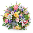 A generous, rounded bouquet of mixed seasonal flowers is shown centred against a bright white background, casting a soft shadow that reveals its domed, carefully sculpted shape. The arrangement feels like a condensed garden, the kind of hand-tied design you might see ready for delivery from Flowers New Barnet on a calm morning. Dominating the composition are garden roses in pastel tones: blush pink, mellow yellow, and soft peach, some fully open with ruffled, layered centres, others in semi-closed stages that suggest gentle movement and growth. Interwoven through the roses are clematis blooms, their petals stretched into elegant stars of white and pale lavender, each one with a defined yellow centre that glows subtly in the light. Adding striking structure, blue eryngium - sea holly with pointed, thistle-like heads and metallic blue-grey hues - punctuates the softness, lending a modern twist to the otherwise romantic mix. Rich purple lisianthus appear in varying stages of bloom, from tightly wrapped buds to more open, frilled flowers, adding depth and a velvety richness of colour. Bright clusters of red hypericum berries are tucked among the petals, offering small, glossy spheres that stand out vividly against the pastel tones. Surrounding and supporting the blooms is an abundance of foliage: broad, shiny leaves that ground the design, delicate, feathery greens that add lightness, and touches of darker, almost burgundy foliage that create subtle contrasts. The lighting is even and natural, with no harsh shadows, so every texture-from rose petal to thistle spike-is clearly defined. This bouquet conveys warmth and thoughtful intention, making it suitable as a centrepiece, a celebration gift, or a comforting arrangement delivered to families and friends in and around New Barnet.
