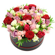 A round black hat box trimmed delicately in red is captured in sharp focus against a white backdrop, overflowing with a meticulously shaped dome of roses that appears almost cloud-like in its fullness. The arrangement celebrates colour and contrast: deep crimson roses convey classic romance, layered alongside tender blush pinks and lively fuchsias that add a playful lift. Cream and white roses brighten the composition, their petals soft and luminous, while peach and coral tones bring a gentle, sun-warmed glow to the mix. Threaded among them, lavender and mauve roses introduce a graceful, vintage note, like the last light over New Barnet rooftops at the end of a calm day. Each bloom looks freshly cut, some roses fully open with petals curling back to reveal their hearts, others still forming tight, rounded buds that promise long-lasting beauty. Clusters of spray roses tuck between the larger heads, filling any gaps and creating an intricate, layered surface that feels lush but never heavy. Fine, glossy green leaves are scattered throughout, breaking up the colour with fresh flashes of foliage that frame and support the blossoms. The overall effect is one of refined abundance, as though this hat box has just been delivered to a doorway near Oakleigh Road North or a townhouse close to New Barnet station. It's an image of a premium floral gift designed to celebrate love, birthdays, or special family moments, full of texture, fragrance, and heartfelt intention.