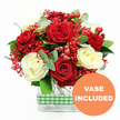 A richly detailed, festive bouquet of red and white roses is presented against a bright white background, photographed in a style that makes it feel as though it is glowing under soft daylight in a New Barnet home. At the centre, deep red roses and creamy white roses open fully, every petal curved and layered, creating a lush tapestry of colour that shifts subtly between warm crimson and gentle ivory. Around and between these roses, tiny red filler flowers, reminiscent of tinted baby's breath, scatter like fine lace, adding a delicate, airy counterpoint to the more substantial blooms. Glossy red hypericum berries, rounded and firm, punctuate the arrangement, their jewel-like shine evoking a festive mood that would fit perfectly with winter celebrations or romantic evenings near New Barnet's High Road. The bouquet is wrapped in a collar of verdant foliage, where silvery eucalyptus sprigs and broader green leaves weave together to give both height and structure, suggesting the hand of an experienced florist shaping each stem with care. All of this is anchored in a clear, rectangular glass vase, through which the stems are neatly visible, reinforcing the clean, contemporary style of the design. A green and white gingham ribbon encircles the midsection of the vase, its checked pattern adding a homely, rustic charm as if it has been tied just before delivering to a New Barnet doorstep. In the bottom right corner of the image, an orange circular badge announces VASE INCLUDED in crisp white letters, making it clear that the bouquet arrives ready to display straight from the box-ideal for anniversaries, Valentine's surprises, or simply brightening a lounge or office across New Barnet.