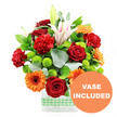 Captured against a pure white background, this exuberant floral arrangement radiates warmth and celebration, as if prepared for a special gathering in a New Barnet townhouse or a sunlit flat near Victoria Park. The bouquet is designed in a sleek, rectangular clear glass vase, which showcases the neatly arranged stems and clean lines of the composition. Around the base of the vase, a soft light green and white gingham ribbon wraps like a tailored belt, introducing a gentle, country-inspired accent that contrasts with the modern glass. The flowers themselves are a carefully considered mix: velvety deep red roses with layered, spiralling petals sit alongside plush red-orange carnations, their softly frilled edges giving a sense of movement and fullness. Bright orange gerbera daisies, each with a strong dark central eye, add an almost playful burst of colour, like little suns scattered throughout the design. Elegant white Oriental lilies emerge above the main cluster; some are fully open, displaying pale pink stripes and delicate stamens, while others are still in bud, adding height and a promise of further blooms in the days ahead. Nestled throughout are small, spherical lime green pompom chrysanthemums whose rounded forms and vivid colour create a lively contrast to the larger blossoms. Supporting this colourful array is a base of rich greenery, including broad, glossy deep green leaves and airy stems of silver-green eucalyptus that arc gently outward. In the lower right corner, a circular orange badge partially overlaps the image, boldly inscribed with VASE INCLUDED in clear white capital letters, signalling that the arrangement arrives complete and ready to display-perfect for birthdays, congratulations, or simply delivering a burst of cheer to someone in New Barnet.