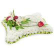A tender, pillow-shaped floral tribute composed entirely of small, pristine white chrysanthemums, photographed against a clear white background. The rectangular cushion is densely planted with tight, soft chrysanthemum heads so close together they read as a single plush, cloud-like surface-cool to the eye and comforting to imagine beneath the hand. A pleated trim of pale lime-green satin ribbon frames the cushion's edge, the slight sheen and folded frill catching soft light and adding a gentle, refined border. At the upper left a naturalistic cluster rises: two open white Oriental lilies, their waxy petals curving back to reveal pale yellow stamens, beside a graceful closed lily bud that promises fragrance; intermingled are deep burgundy spray carnations whose ruffled blooms give warmth and visual weight against the white field. Lush green foliage-delicate ferns, broader salal-like leaves and varied greenery-creates depth and a living backdrop for the focal group. From that cluster a slender, arching loop of natural green bear grass or decorative wire sweeps across the pillow to the right, ending in a single deep-red rosebud poised on the surface; its velvety petals are just beginning to unfurl, a solitary emblem of lasting love. The overall palette of immaculate white, soft lime-green trim and rich red accents reads as purity, quiet dignity and heartfelt remembrance. This classic sympathy cushion, imagined for a wake or funeral, is composed with the respectful restraint often requested for local services in New Barnet and neighbouring Brunswick Park, where families favour floral tributes that speak of peace and memory.