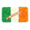 A beautifully crafted Irish flag funeral tribute is shown lying flat against a bright white background, its colours vivid and carefully defined. The design is composed of hundreds of closely packed flowers arranged in three equal vertical sections, forming a soft, cushion-like rectangle. On the left, a bold band of green chrysanthemums and similar small-petalled flowers creates a dense, velvety surface that feels rich and grounded, much like the green spaces dotted around New Barnet. In the centre, a pristine strip of white blooms offers balance and calm, their delicate petals blending into a seamless, snowy band that suggests purity, remembrance, and quiet prayer. On the right, a lively band of bright orange flowers brings gentle warmth and energy, echoing the glow of streetlights after dusk along East Barnet Road. Cutting diagonally across the white and orange sections, from lower left to upper right, is a glossy coral-red ribbon. The ribbon is smooth and slightly reflective, and across it the word GRANDAD appears in bold, silver block letters, proudly announcing the tribute's purpose as a farewell to a much-loved Irish grandfather. Small, neat white pins secure the ribbon to the floral surface, revealing the careful handiwork behind the arrangement. The overall effect is dignified and heartfelt, a meaningful choice for a funeral or memorial service in New Barnet, where families wish to honour both personal memories and Irish roots through a single, lovingly made floral design.