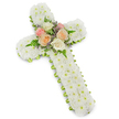 A traditional white funeral cross, thoughtfully arranged from fresh flowers, is set against a bright white background that allows its shape and texture to stand out clearly. The cross is completely covered with small white button chrysanthemums, placed so closely together that they form a dense, even layer of petals from end to end. This plush covering follows the contours of the long vertical beam and shorter arms, creating a classic Christian cross silhouette that radiates serenity and purity. Along the entire perimeter, a slim band of lime green ribbon provides a neat border, its cool, citrus tone echoing the crisp greenery seen in the gardens and tree-lined streets of New Barnet. This ribbon edge adds just enough colour to gently frame the design, while keeping the mood soft and reverent. At the central meeting point of the cross, a delicate grouping of roses adds a focal accent. Open blooms in creamy white, soft blush pink, and gentle peach sit together, their layered petals surrounded by light, feathery fern fronds and tiny stems of lavender-tinted filler blossoms. The interplay of white, green, pink, peach, and lilac tones creates a peaceful balance, symbolising hope and tender remembrance. The overall arrangement appears carefully balanced and meticulously crafted, suitable for display at a church, crematorium, or graveside service in the New Barnet area. It conveys a message of sympathy, Christian faith, and enduring love, offering a visually calm, comforting presence for family and friends saying a final goodbye.