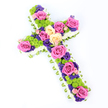 A large floral cross, designed as a traditional Christian tribute, is photographed on a bright white background that makes every colour stand out in crisp detail. The cross is evenly proportioned, its arms and base outlined by a deep border of white spray chrysanthemums that form a soft, cushion-like frame. Peeking just beyond this white fringe is a narrow band of pale green ribbon or carefully folded foliage, adding a gentle hint of springlike freshness and giving the design a neatly finished edge, much like a carefully pressed ribbon on a ceremonial robe. Within this border, the interior of the cross is a vibrant garden of colour, suitable for a funeral or memorial in New Barnet where families wish to blend respect with a celebration of life. Large roses in vivid fuchsia pink and gentle creamy yellow dominate the design, their open blooms revealing spirals of velvety petals that suggest tenderness and enduring love. They are interspersed with lively lime-green button chrysanthemums, their compact, spherical heads adding a playful, contemporary twist to the otherwise classic tribute. Woven among these larger focal flowers are small, deep purple blossoms-likely statice or lisianthus-introducing rich, jewel-like shadows that balance the brightness of the pinks and greens. The cross is presented at a slight diagonal, which enhances its three-dimensional shape and makes the flowers appear as though they are gently cascading. The lighting is bright and even, with no harsh shadows, allowing every subtle hue and texture to show, from the ruffled white edges to the glossy green ribbon. This floral cross would feel at home in a peaceful New Barnet chapel or at a quiet graveside service, offering a message of remembrance, hope, and gentle comfort.