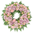 This image shows a generous, circular sympathy wreath set against a clean white background, photographed from directly above so its perfect ring is clearly defined. The design feels calm and composed, built around lush, fully bloomed roses in muted lavender and soft mauve shades, their petals opening in layered whorls that create a plush, velvety surface. Scattered between these larger flowers are clusters of delicate blush pink spray roses and small buds, some just starting to open, which bring a sense of softness and quiet hope to the arrangement. All of the blooms are anchored on a thick bed of deep green fern fronds, the finely toothed leaves radiating outward to form a natural frame that is both structured and gently feathery, reminiscent of foliage you might spot in the green spaces around New Barnet. Here and there, darker sprigs of foliage and minute filler buds nestle between the petals, adding shadow and depth so the wreath appears three-dimensional and lovingly hand-crafted. The colours are subtle rather than bright, with the dusty purples, understated pinks, and rich greens working together to convey a mood of respect and serenity. The neutral white background and soft, even lighting focus attention solely on the flowers, making it easy to imagine this wreath resting beside a casket or memorial display at a quiet service in one of New Barnet's churches or funeral homes. It feels like a floral embrace, offering condolences and peaceful remembrance without the need for words.
