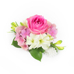 Set against a pristine white background, this compact, corsage-like arrangement reads as a study in refined romance and tactile contrast. At its centre sits a plush, fuchsia-pink rose whose tight inner petals curl gently outward, velvet to the touch and catching soft, natural light so that subtle shifts of magenta and rose-red play across each layer. Encircling the rose are clusters of pale pink and lavender hydrangea florets; their papery, cloud-like petals add volume and a gentle, nostalgic softness that cradles the central bloom. Two creamy white, trumpet-shaped blossoms-small amaryllis or lily-like alstroemeria-nest below the focal rose, their pale throats edged with a cool green that brightens the composition and introduces a whisper of purity. Deep, glossy green leaves fan out at the base, their broad surfaces reflecting a hint of sheen and anchoring the arrangement with a fresh, garden-scented presence. From either side, slender green buds tipped with a soft yellow introduce vertical movement and the promise of future opening. At the lower right, a delicate cluster of luminous white pearls, differing slightly in size, cascades like a quiet accent, lending the piece a vintage bridal whisper without overwhelming the flowers. The overall light is bright but gentle, as if lit by morning sun through a nearby window, enhancing textures and the cool, floral fragrance imagined on the skin. This arrangement feels suited to a wedding corsage, a prom accessory, or a small, intimate gift celebrating anniversaries or milestone moments in and around New Barnet, its charm quietly echoing the neighbourhood's leafy streets and local gatherings.