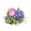 Pinned against a clean white background, this compact corsage reads like a small love letter in bloom - its focal rose half-open, petals melting from a gentle lavender-pink at the core to a lively fuchsia at the outer ruffle. Beside it, a tight cluster of indigo-purple florets, recalling garden hydrangea, each bears a luminous blue center rimmed with a bright yellow-green eye, giving the piece an almost jewel-like sparkle. The flowers are cradled in a thoughtful mix of foliage: glossy variegated ivy with deep emerald hearts and sunny lemon-yellow margins, soft silvery-green leaves that suggest lavender foliage, and a sculptural green-and-cream striped blade curled with elegant intent. Airy, feathery sprigs of lighter green-like asparagus fern-are threaded through the composition to add lift and a gentle, whispery texture. Below, a fine web of deep purple mesh peeks out, providing depth and a modern, slightly shimmery backdrop that sets the colours aglow under soft studio light. On the lower right a short strand of small white pearls suggests a wristlet or refined fastening, catching the eye with a classic nod to tradition. The overall effect is both romantic and contemporary, suited to a bride, prom-goer, or guest seeking a delicate but confident floral accent. As a florist who often fits corsages for ceremonies and formal evenings around New Barnet and nearby Brunswick Park, I imagine this piece pinned to a lapel or gently fastened at the wrist - a tactile keepsake that brings scent, texture and a quiet joy to any special moment.