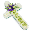 A dignified floral cross tribute is shown from above against a clean white background, its design combining classic funeral symbolism with a fresh, contemporary colour palette ideal for services in and around New Barnet. The arms and body of the cross are completely covered with closely packed white spray chrysanthemums, creating a plush, cushion-like appearance with soft, feathery petals that suggest quiet peace. A vivid green ribbon neatly borders the entire outline, sharply defining the shape and adding a lively yet respectful contrast. Running along the centre of the cross's vertical arm is a deliberate stripe of lime green button chrysanthemums, their small, rounded heads forming a smooth panel of colour. Over this central section, thin pale green wires are gently draped and crossed in a delicate, almost net-like pattern, offering a touch of modern detail. At the intersection of the cross, a compact but striking cluster of deep purple lisianthus blooms provides a rich focal point. The velvety, ruffled petals of the lisianthus are paired with bright lime green chrysanthemum buttons, repeating the accent colour of the vertical stripe. Behind the central cluster, dark green fern fronds and foliage extend outward, adding depth, softness, and a hint of natural wildness that contrasts with the structured shape of the cross. The lighting is even and clear, highlighting every nuance of the textures and colours. This floral cross is a thoughtful choice for Christian funerals, memorial services, or graveside tributes within the New Barnet area, conveying condolences, faith, and lasting remembrance in a gentle, visually soothing way.