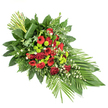 An elongated funeral spray in deep red and vivid green is shown on a plain white background, its gentle teardrop shape leading the eye from a tall accent of greenery at the upper left down to a softly spreading fan of leaves at the lower right. At the heart of this tribute lies a generous cluster of deep red roses, their velvety petals ranging from tightly furled buds to fully open blooms, symbolising love that spans time. Among them nestle bright red gerbera daisies with dark centres and frilled red carnations, creating a varied tapestry of petal shapes and textures. Threaded throughout this rich red base, lime green button chrysanthemum pompons stand out with almost neon clarity, their small, spherical heads adding a clean, contemporary feel that brightens the composition without diminishing its solemn character. Tiny white filler flowers, possibly daisies or gypsophila, are sprinkled lightly between the larger blooms, bringing a soft, airy counterpoint to the bold colour contrasts. The flowers are cradled in an abundance of fresh foliage: broad, glossy dark green leaves like salal provide a sturdy foundation, while feathery leatherleaf fern and other textured greens add layers of movement and depth. At the lower right, long, strap-like leaves fan out to extend the line of the spray, while at the upper left a neat bundle of tall green stems rises vertically, wrapped at the base with one elegant broad leaf. This thoughtful, dignified design, suitable as a casket spray or standing tribute at a New Barnet memorial service, conveys respect, remembrance, and heartfelt condolence through its carefully balanced colours and forms.