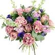 Captured against a bright white backdrop, this bouquet feels like a quietly luxurious moment frozen in time, as if it has just been arranged on a worktable in New Barnet and carefully lifted into view. At its heart, generously petalled garden roses in blush pink and vintage mauve unfurl in soft spirals, radiating classic romance. They are encircled by ruffled carnations whose petals gently ripple from creamy, pale centres to rose-pink and plum edges, creating a soft, almost fabric-like texture that invites you to imagine how velvety they feel to the touch. Striking notes of colour come from deep indigo and royal blue flowers: an open anemone with a dark, near-black centre sits proudly near the front, while smaller, tulip-shaped buds in similar tones peek through the pinks like scattered gemstones. Wisps of pale lilac and soft lavender stock rise above and between the larger blooms, their clusters of tiny flowers adding movement and a light, powdery fragrance reminiscent of spring evenings near Hadley Wood or around New Barnet's tree-lined streets. Embracing the flowers is a collar of foliage-silvery eucalyptus with rounded leaves interlaced with darker green stems-that lends freshness, structure, and a hint of cool, herbal scent. The stems are neatly bound and visible at the base, signalling a freshly hand-tied arrangement ready to slip into a favourite vase as soon as it's delivered to a doorstep off East Barnet Road or a cosy flat near the station. The mood is tender and reflective, ideal for anniversaries, heartfelt birthday wishes, or simply letting someone know they are cherished without needing many words.