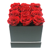 In this striking studio-style image, a minimalist yet opulent floral design is showcased: twelve rich red roses, likely preserved for longevity, are packed with precision into a sleek, matte black square box, a look increasingly popular with New Barnet customers who favour clean, modern lines. The camera meets the arrangement at eye level, so the perfectly organised 3x4 grid of blooms commands full attention. Each rose is in full, open form, with layer upon layer of velvety crimson petals swirling towards a gently shadowed centre, their uniform height creating a smooth, almost cushion-like surface that just crests above the rim of the box. The container is smooth and untextured, its edges sharply defined, and a single slim white band wraps horizontally around its lower section, like a refined trim on a tailored garment, adding a quiet note of sophistication. The photograph is set against a pure white backdrop, with no additional props, much like a carefully staged product shot you might imagine in a boutique close to New Barnet station or along the High Road. Soft, even lighting ensures that every petal is clearly visible, with delicate shadows accentuating the folds of the roses and the geometry of the box without any harsh highlights. The overall impression is of understated luxury and enduring romance, making this image ideal to represent a preserved rose gift delivered for an anniversary dinner in New Barnet, a Valentine's surprise in a flat near Barnet Playing Fields, or a thoughtful, long-lasting token of affection sent through a local, same-day flower delivery service.