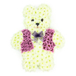 In this detailed funeral tribute, a three-dimensional teddy bear made from fresh flowers appears almost ready for a gentle cuddle, bringing a sense of innocence and warmth to a solemn occasion in New Barnet. The bear is meticulously constructed from creamy white chrysanthemum blooms, each flower head aligned so closely that they form a continuous, plush-like surface over the bear's head, rounded belly, ears, arms, and legs. The chrysanthemums create a soft, rippling texture, and their subtle ivory tones stand out crisply against the bright, uncluttered white background, focusing all attention on the figure itself. The facial features are small but expressive: two dark, button-like eyes sit symmetrically on the rounded face, while a slightly larger dark bloom marks the nose, with a gentle curve of petals below that hints at a tender, reassuring smile, like a familiar toy resting on a child's bed in a home just off Station Road or closer to Victoria Park. Across the teddy's chest, a waistcoat crafted from vivid purple and mauve petals introduces rich colour and structure, with carefully defined lapels and panels that give the impression of a tiny tailored garment. At the neckline, a soft, lavender mesh bow tie sits neatly in place, its see-through loops softening the transition between the vest and the creamy floral fur. Though the image cannot convey scent, one can almost imagine the faint, green freshness of recently cut stems and petals prepared for a local New Barnet service. This floral teddy bear arrangement is a poignant, personalised sympathy tribute, conveying love, remembrance, and comfort at funerals, children's memorials, and graveside tributes throughout the New Barnet community.